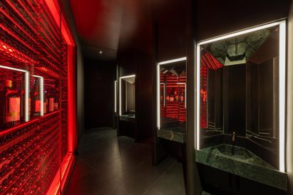 A glowing red wine rack forms a partition for a restaurant bathroom, which features green marble basins