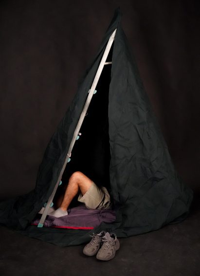 Photo of a tent structure fashioned from a ladder and a sheet with a person's legs sticking out from inside