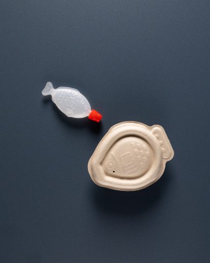 Photo of a classic plastic soy sauce fish next to the bigger bagasse pulp compostable packaging by Heliograf and Vert Design