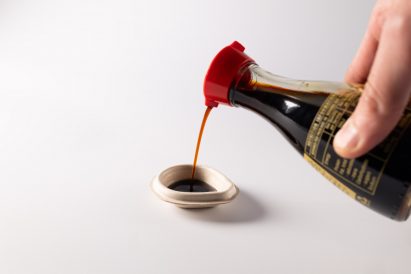 Close-up photo of a small plant-pulp cup being filled by a kikkoman soy sauce bottle