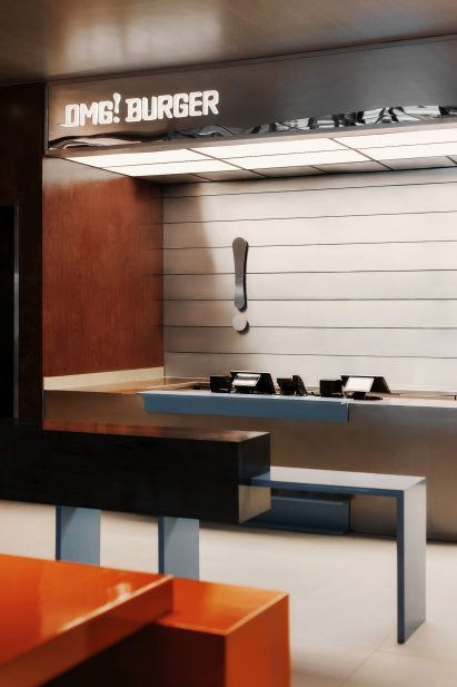The OMG! Burger logo glows above a service counter, while the exclamation point is repeated behind the registers