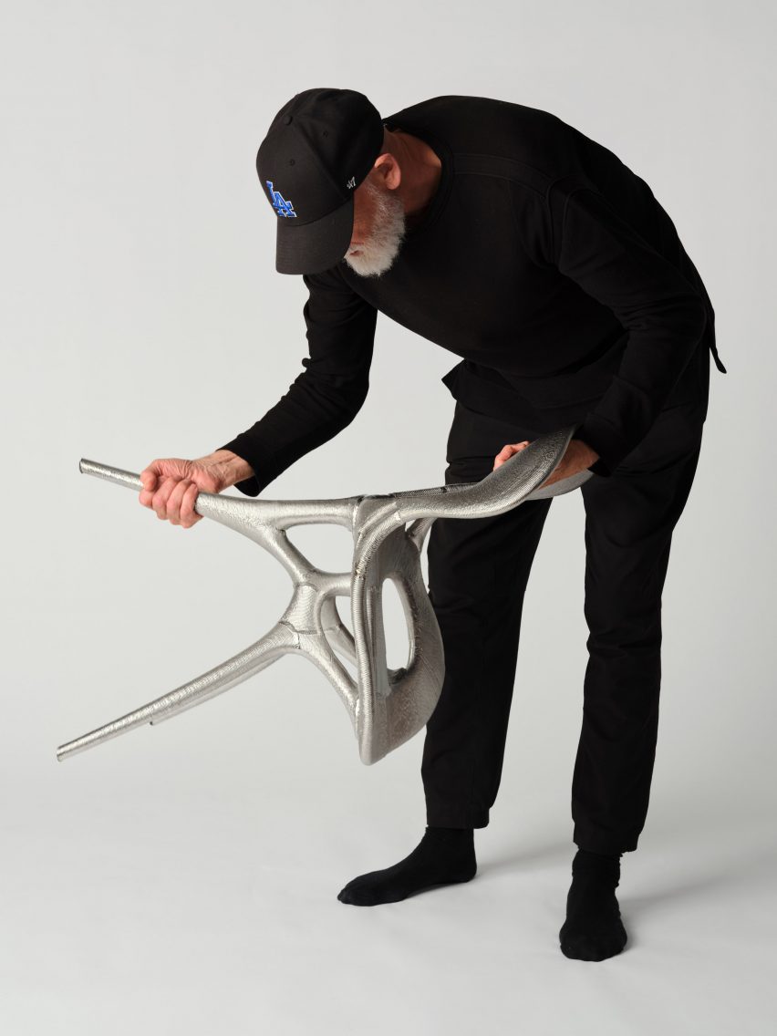 Photo of Ross Lovegrove handling the metal chair he co-created with Google DeepMind and Modem