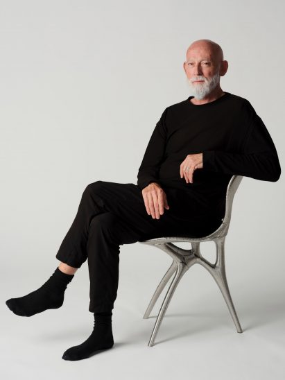Photo of Ross Lovegrove sitting in the metal 3D-printed chair he created with Google DeepMind and Modem