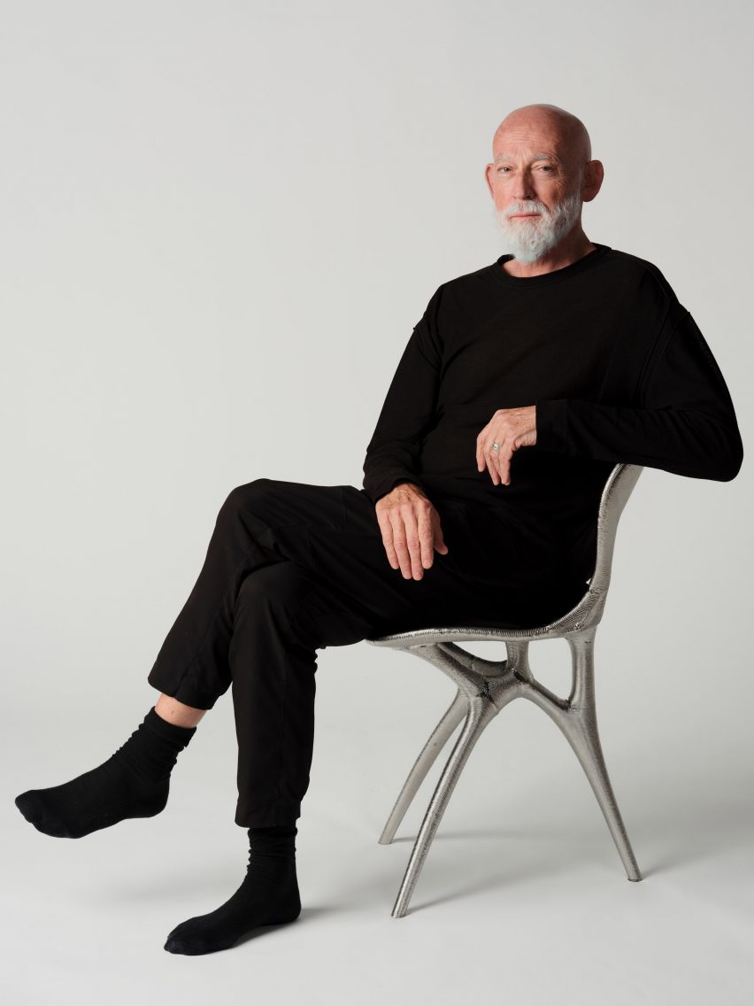 Photo of Ross Lovegrove sitting in the metal 3D-printed chair he created with Google DeepMind and Modem