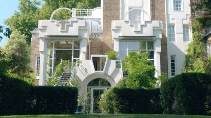 Front view of The Cosmic House in west London, framed by trees and manicured gardens