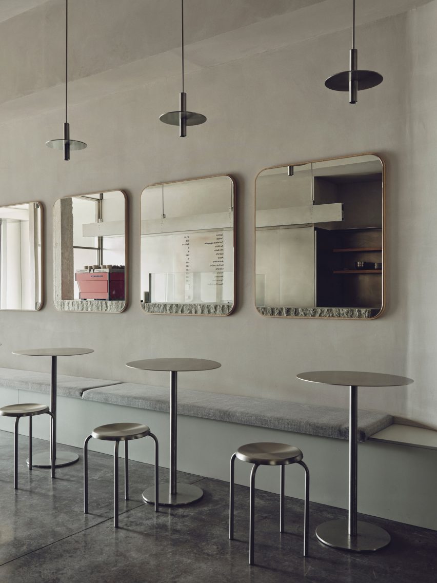 Minimalist cafe seating area with metal tables and stools, grey bench seating, large rectangular wall mirrors, and modern pendant lights.