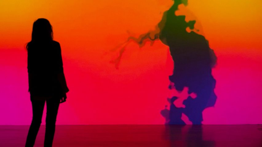 a projection in tones of pink orange and red with a person's silhouette against it
