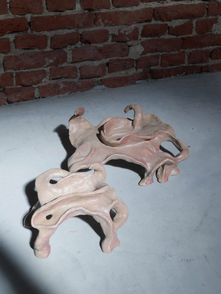 Photo of swirly hand-buitl clay objects that look like abstracted many-legged creatures with a light grey and pink glaze