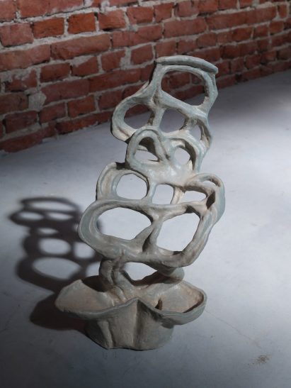 Photo of a clay sculpture made of many loops of chunky clay, twisting around each other to make a loopy web, with a light blue-grey glaze