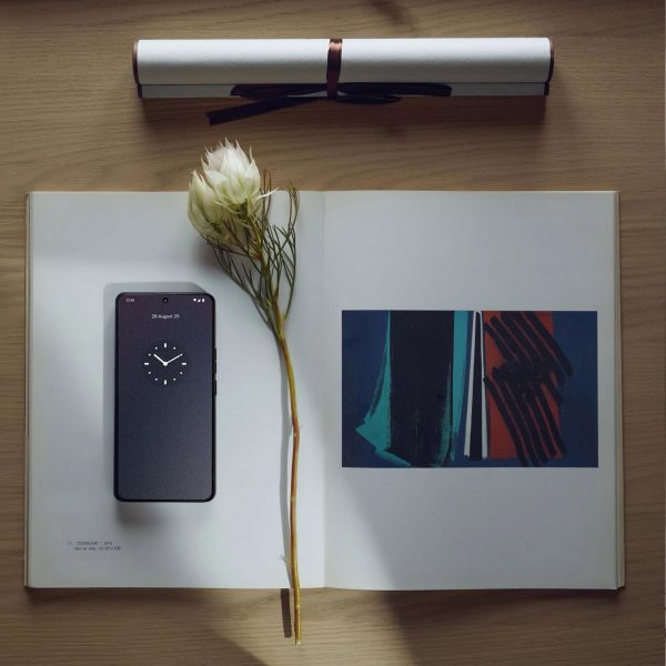 A flatlay image of the Punkt MC03 phone sitting on top of an open book on a desk alongside an elegant white flower