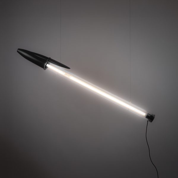 Pen-shaped lamp suspended in front of grey backdrop