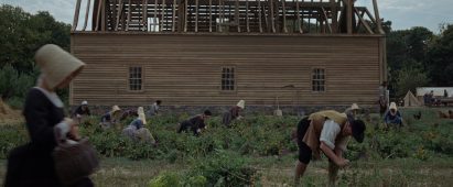 Still from The Testament of Ann Lee showing Shakers labouring under the shadow of a partially built timber-framed building