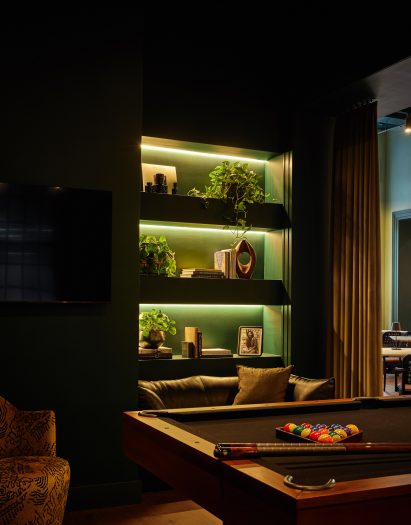 A pool table and large TV screens within a dark green lounge