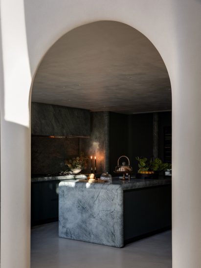 Through a tall white archway is the kitchen. A large marble island takes up the middle of the room.
