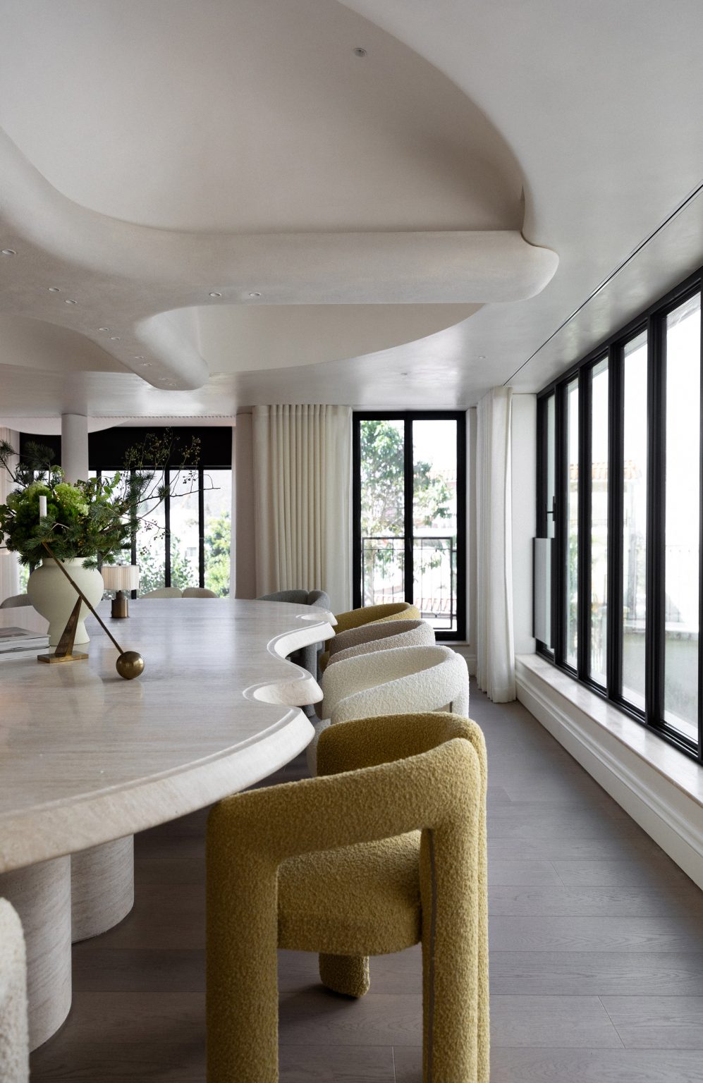 A light room with a white, curved dining table and chairs next to it. There are tall windows along every wall.