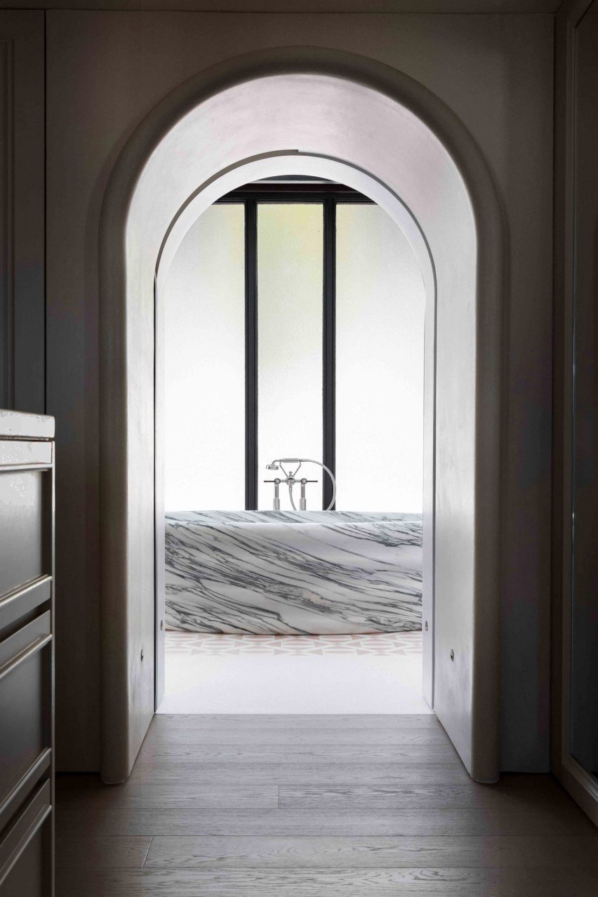 A free-standing marble bath can be seen through a single archway.