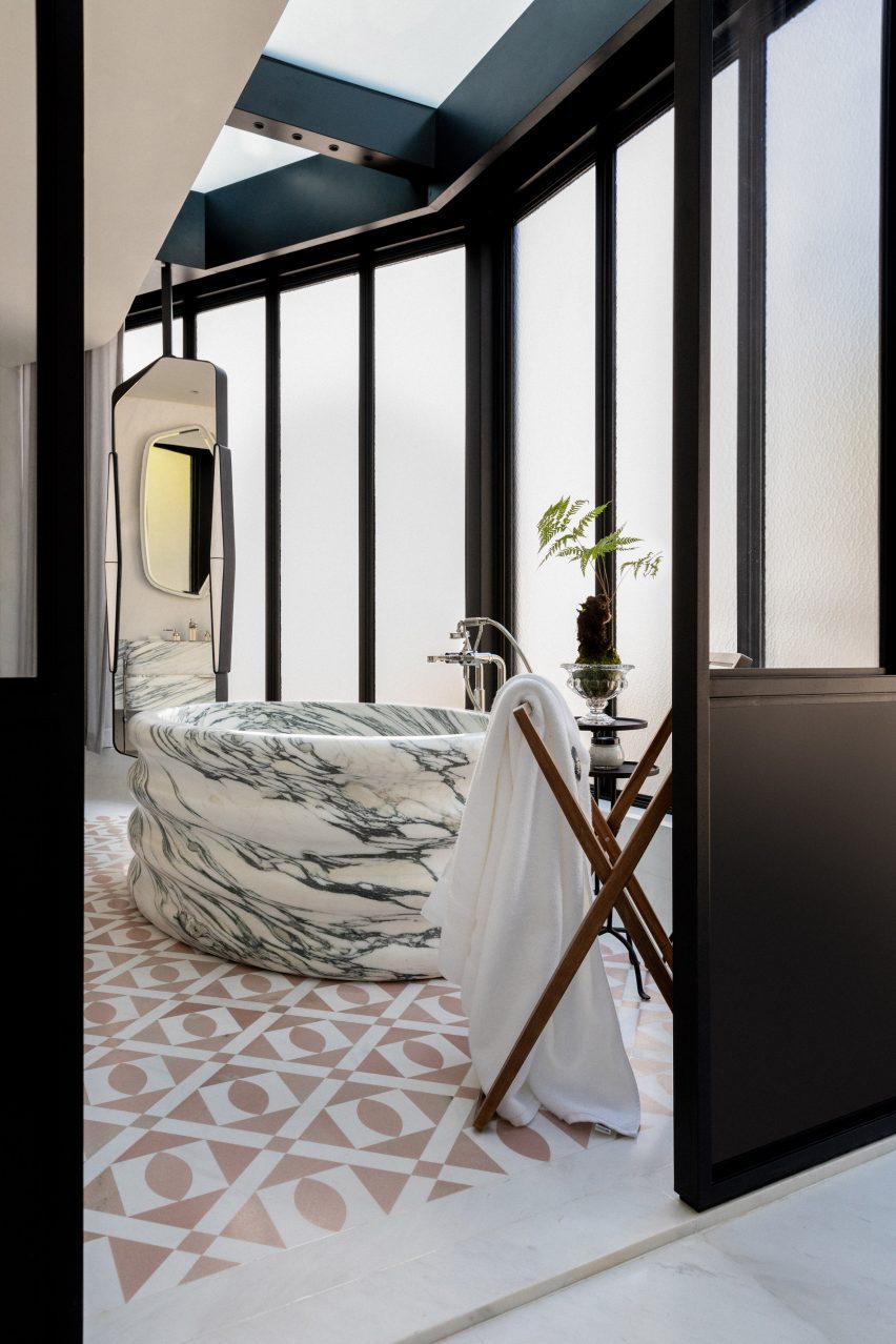 Image of a freestanding marble bathtub surrounded by frosted windows. Light pink, patterned tiles are on the floor.