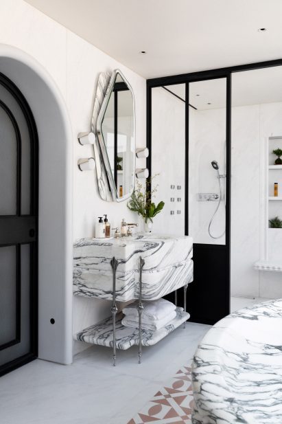 A light bathroom displaying a large, marble sink unit and a shower at the back of the room.