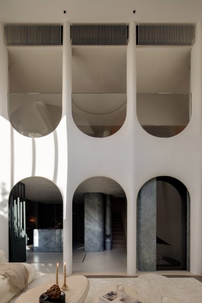 A tall room spanning two floors with three upright archways on the ground floor and three upside down archways showing another room on the upper floor. Through the lower archways, one can see the kitchen.