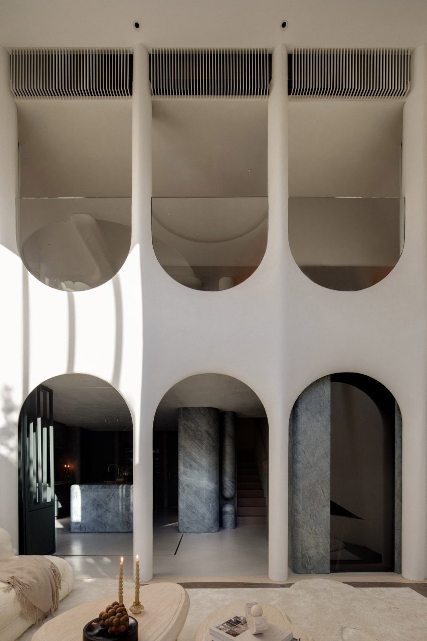 A tall room spanning two floors with three upright archways on the ground floor and three upside down archways showing another room on the upper floor. Through the lower archways, one can see the kitchen.