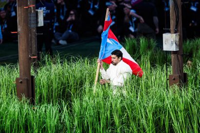 Bad Bunny carrying a Puerto Rican flag through a field of grass