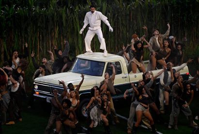 Bad Bunny stood of the rood of a cream-coloured truck, surrounded by dancers