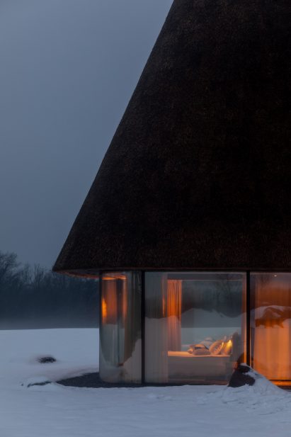 Glass hut with thatched roof in snowy landscape