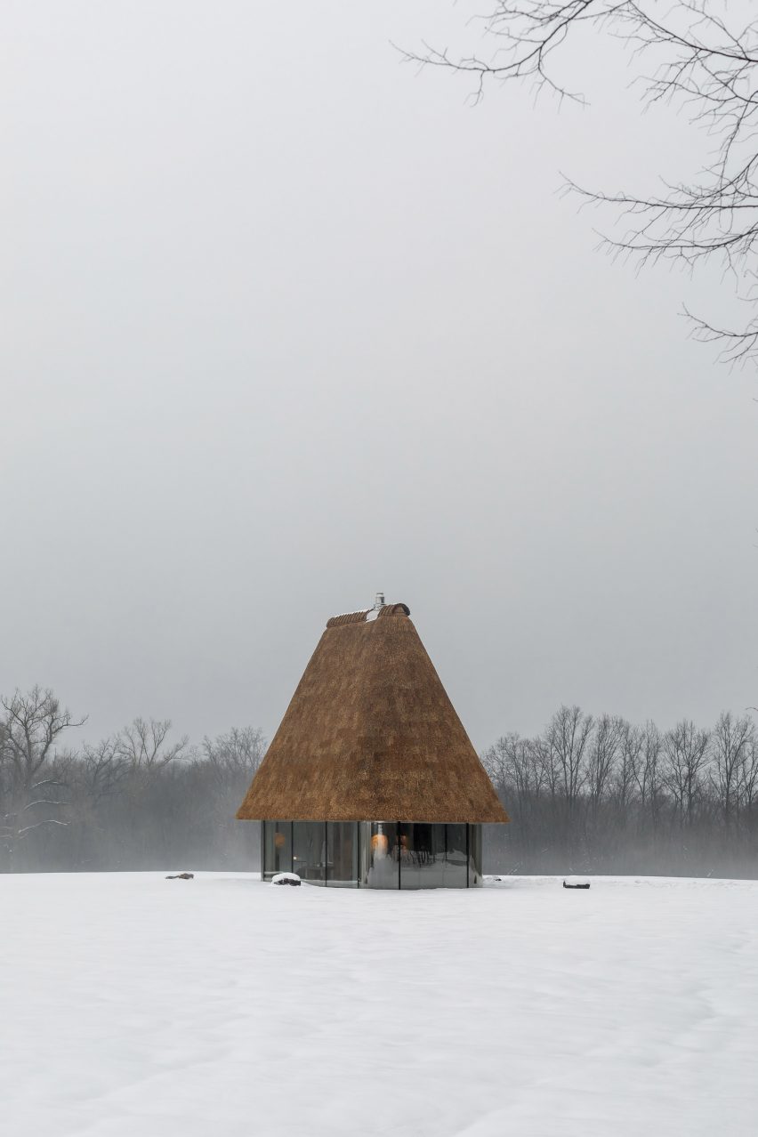 Glass hut with thatched roof in snowy landscape