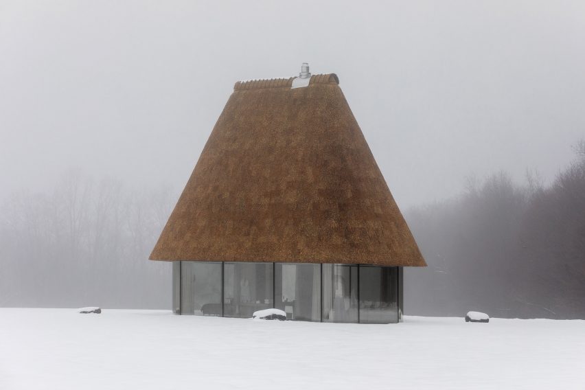 Glass hut with thatched roof in snowy landscape