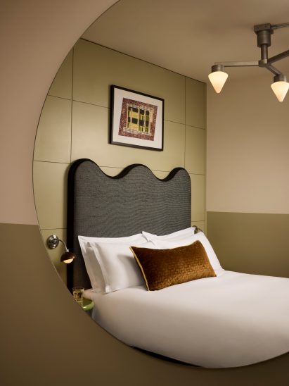 Circular mirror showing bed and painting