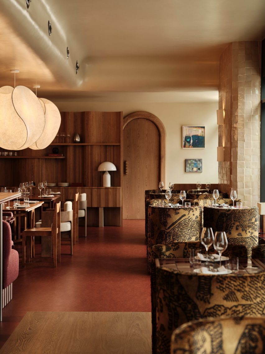 Warm, modern restaurant interior with mid-century design featuring wood-paneled walls, sculptural pendant lights, vinyl record shelving, set dining tables with wine glasses, patterned upholstered chairs, tiled tabletops, red flooring, and cozy ambient lighting in an upscale dining space
