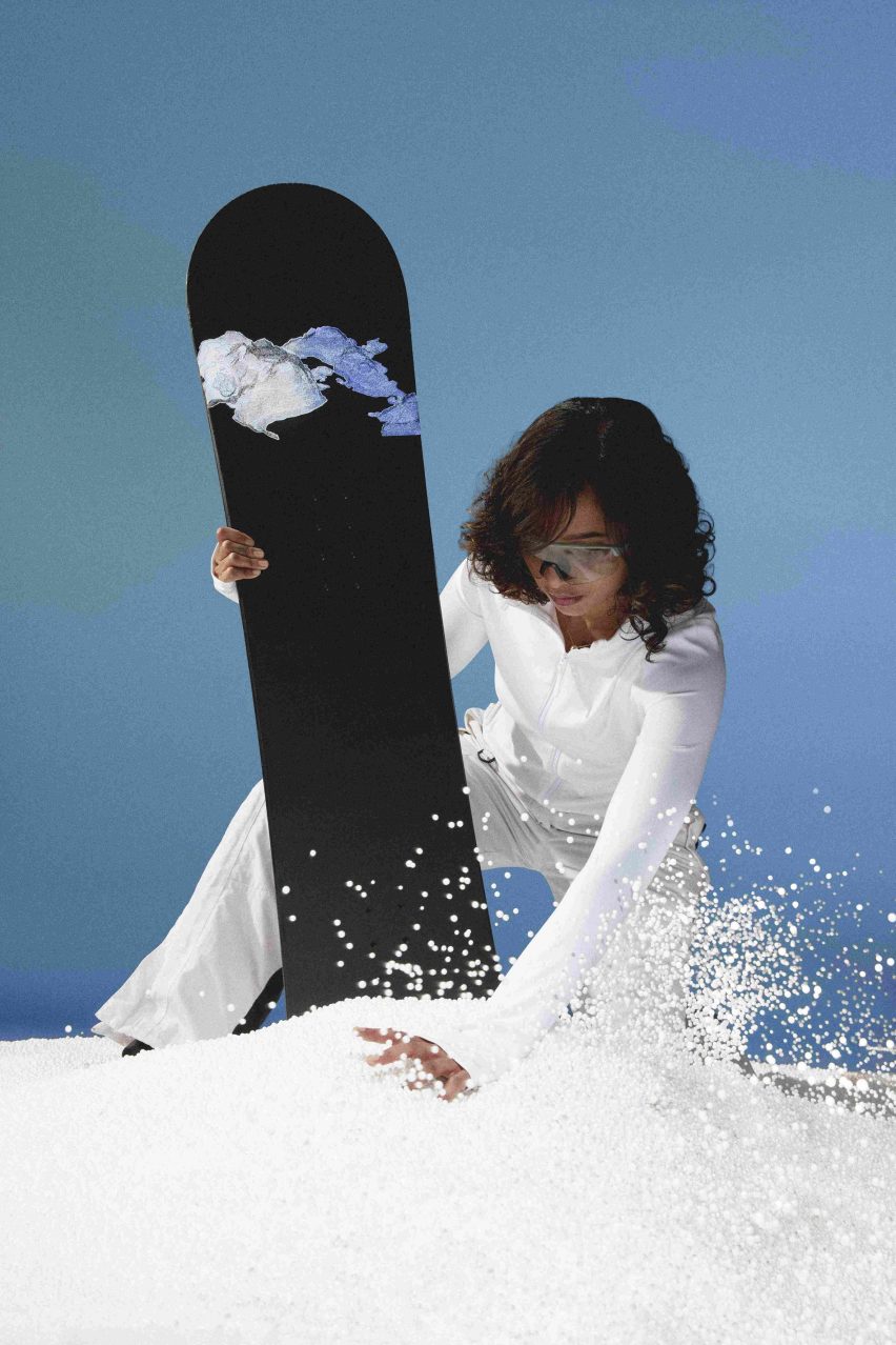 Photo of a woman kneeling in the snow holding a snowboard with a Snow Seeds sticker prototype on it
