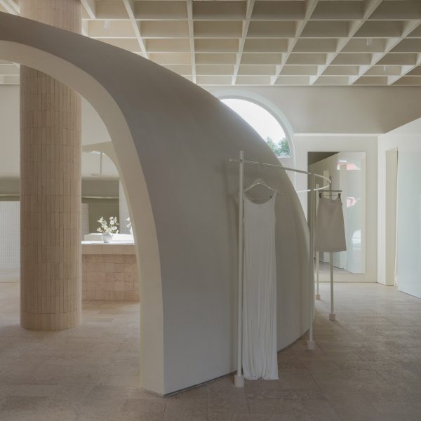 Image of a truncated domed partition wall with arched walkways connecting the main shop floor from a gloss-finished block of changing rooms at the far right of the image. A clothes rail with a hanging dress and skirt wraps around the dome's exterior.