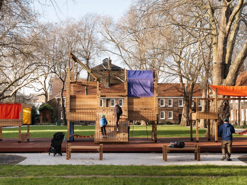 Wide shot of children playing on a wooden playground in a green courtyard of a building
