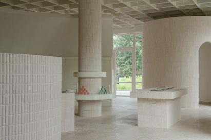 An image of a neutral, cream-toned interior with architectural elements including columns, a cylindrical room and a rectangular table made from travertine and limestone.