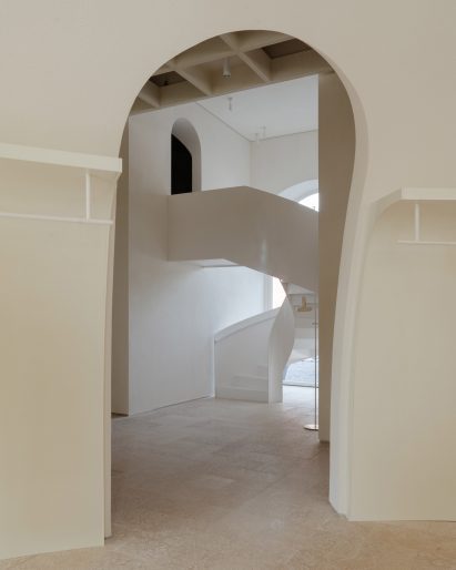 Through a tall archway, we can see a white spiral staircase leading up to another room in the back of the store.