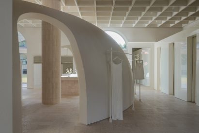 Image of a truncated domed partition wall with arched walkways connecting the main shop floor from a gloss-finished block of changing rooms at the far right of the image. A clothes rail with a hanging dress and skirt wraps around the dome's exterior.