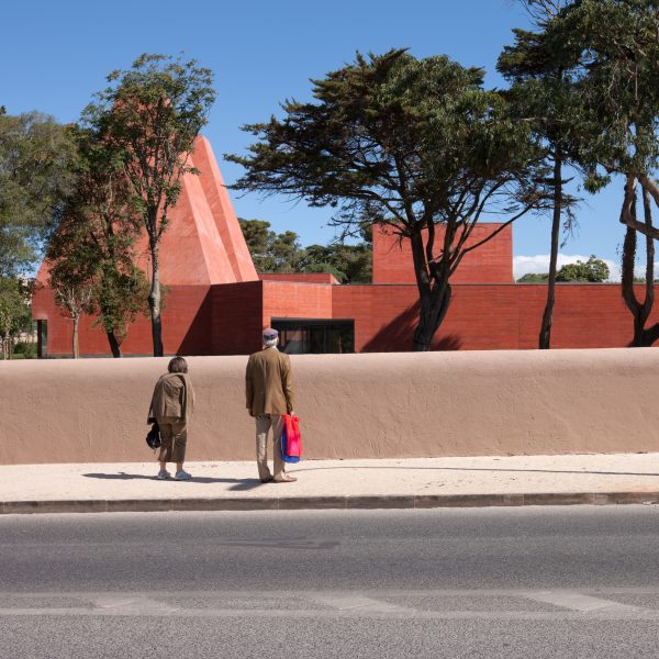 Street view of the museum behind a low wall with visitors looking towards the red concrete building