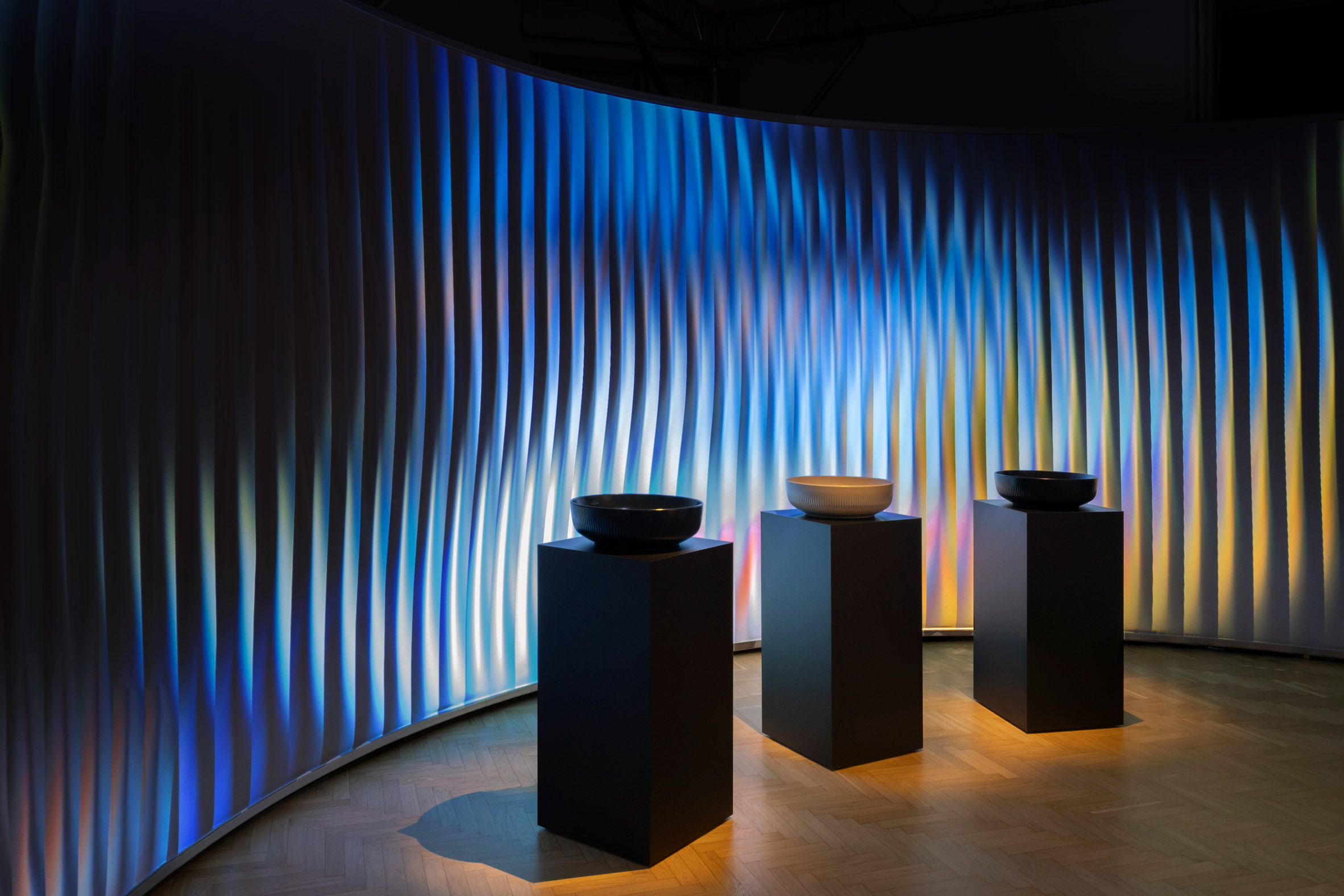 Three basins displayed on black plinths in a dark room with curved walls