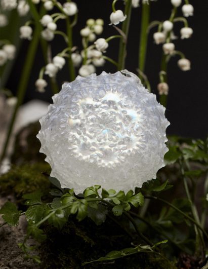 Photo of shimmering iridscent faux flora with a bewitching fractical-like 3D form nestled within a bouquet of greenery and small white flowers