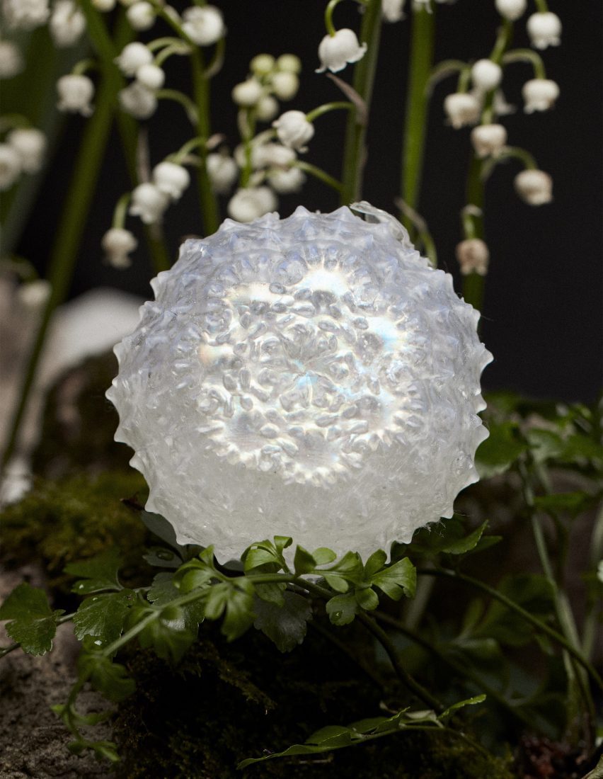 Photo of shimmering iridscent faux flora with a bewitching fractical-like 3D form nestled within a bouquet of greenery and small white flowers