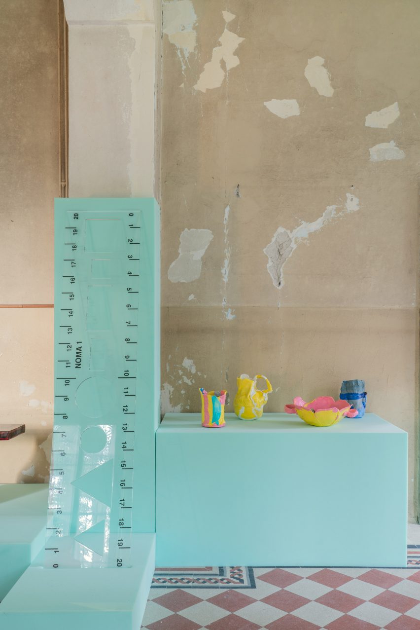 Photo of the House of Creatures exhibition showing an oversized plastic ruler sculpture and several small colourful vessels on mint green foam plinths