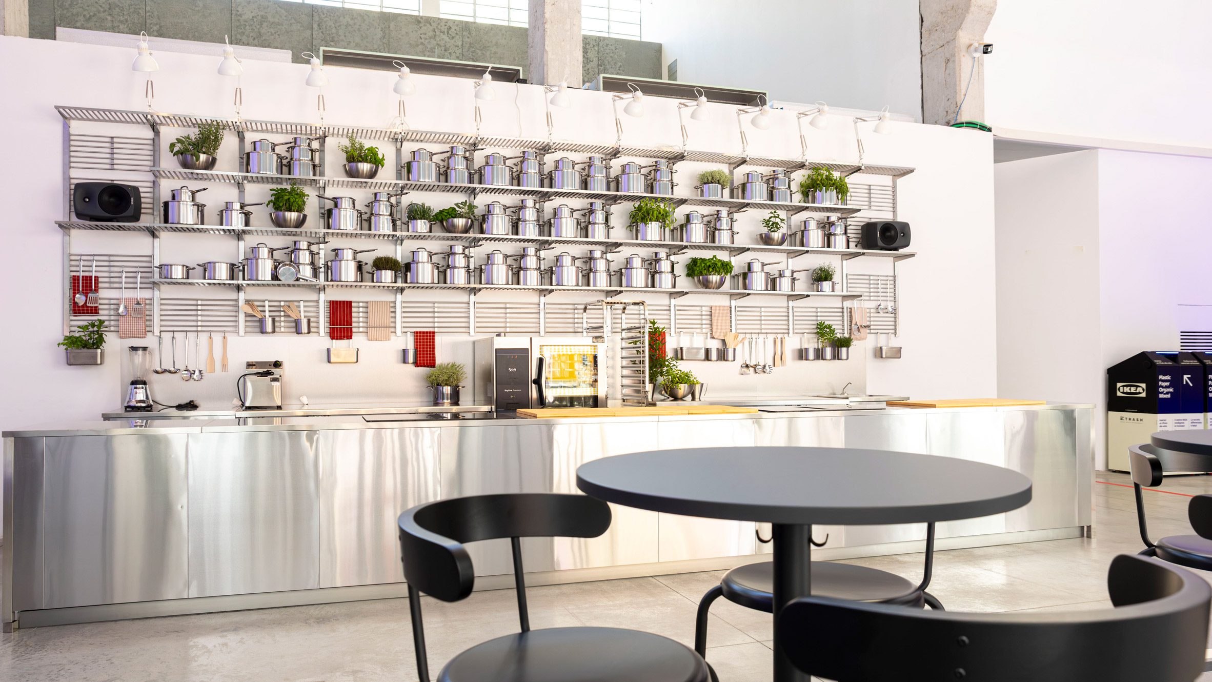 A kitchen wall installation with shelves of stainless steel pots and fresh herbs for IKEA's Food for Thought exhibition in Milan