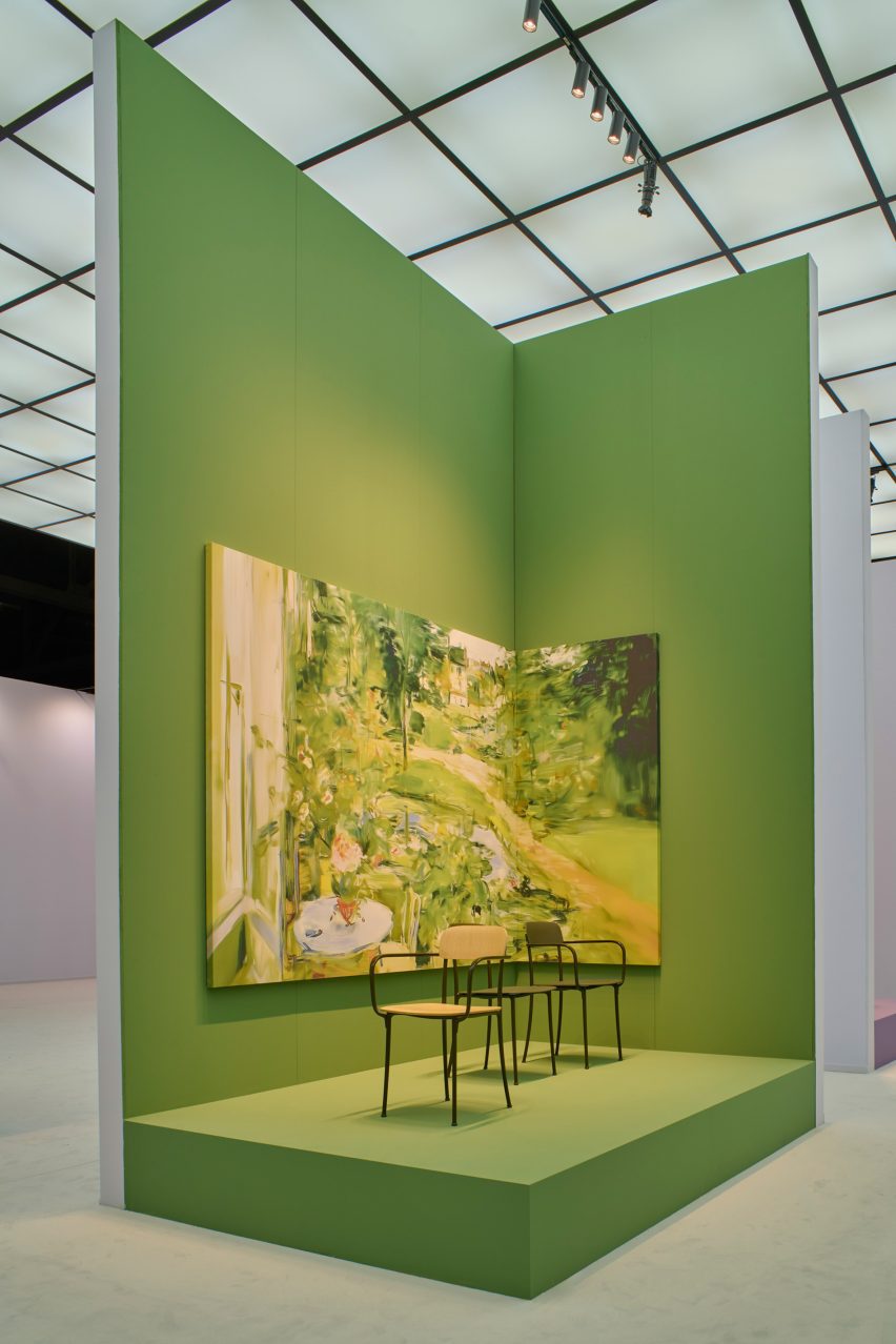 Photo of Barber Osgerby and Kartell's Savoia chair in front of an apple-green backdrop with a painting of a garden scene at its Salone del Mobile 2026 stand