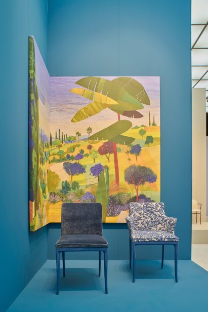 Photo of two Lillybet chairs by Ludovica Serafini and Roberto Palomba and Kartell in front of a cobalt blue backdrop and a large expressionistic landscape painting at the Kartell stand at Salone del Mobile 2026