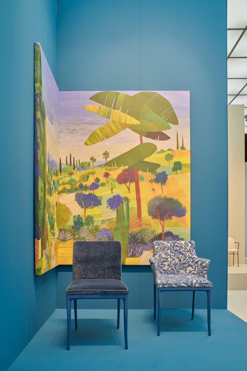 Photo of two Lillybet chairs by Ludovica Serafini and Roberto Palomba and Kartell in front of a cobalt blue backdrop and a large expressionistic landscape painting at the Kartell stand at Salone del Mobile 2026