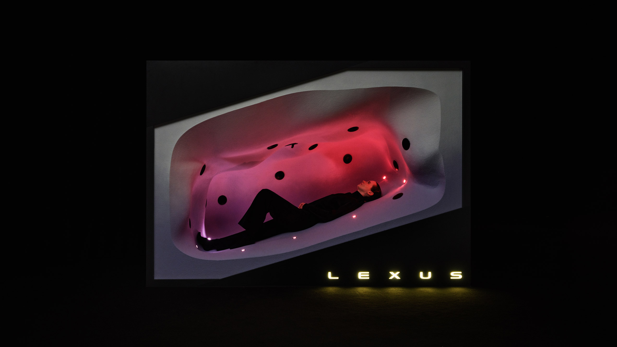 Person reclining inside an enclosed pod lit in pink