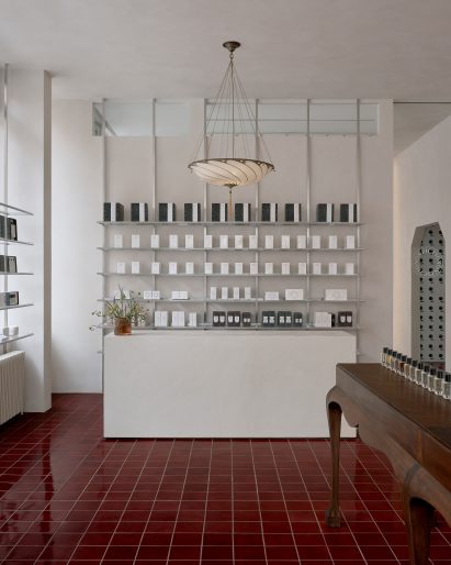 Lime-washed walls and minimalist metal shelving contrasts oxblood tiles inside a perfume store