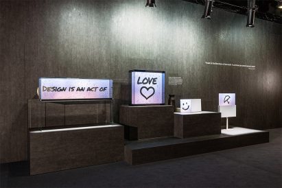 Plinths displaying objects and panels with phrases including "Design is an act of love" in a dark exhibition space