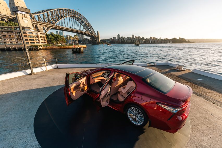 Photo of the Sunburnt Car, a red sedan, with its doors wide open showing its skin-like interior, parked on Sydney's Circular Quay in front of a view of the Sydney Harbour Bridge